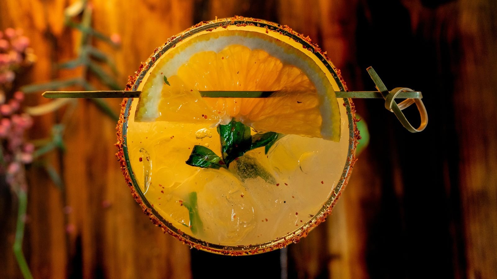 Vista cenital de un coctel con escarchado de tajín, rodaja de naranja y agitador de madera
