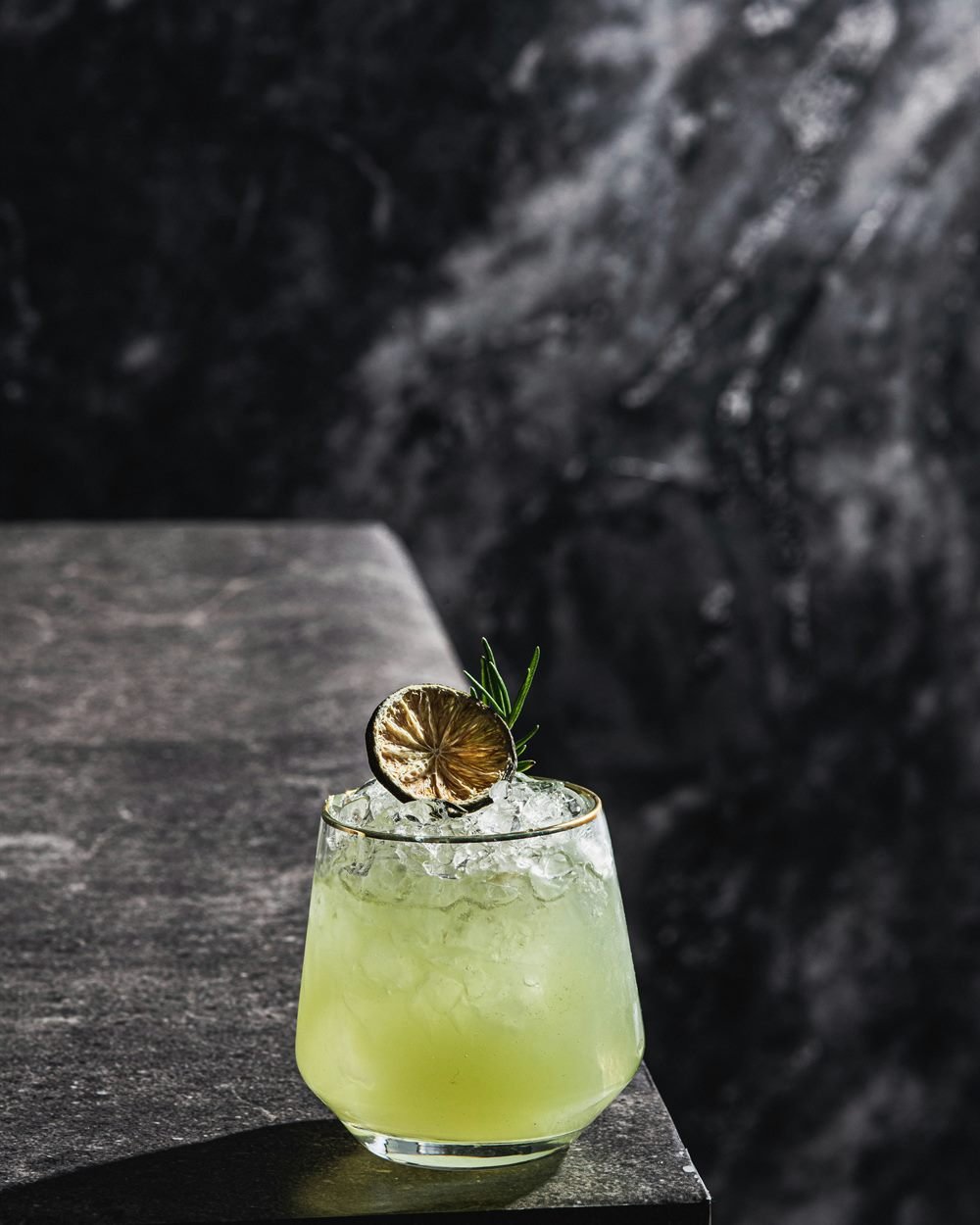 Coctel de autor con limón deshidratado y romero sobre piedra oscura